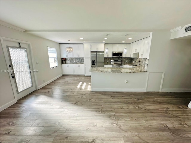 kitchen with white cabinets, kitchen peninsula, appliances with stainless steel finishes, and pendant lighting