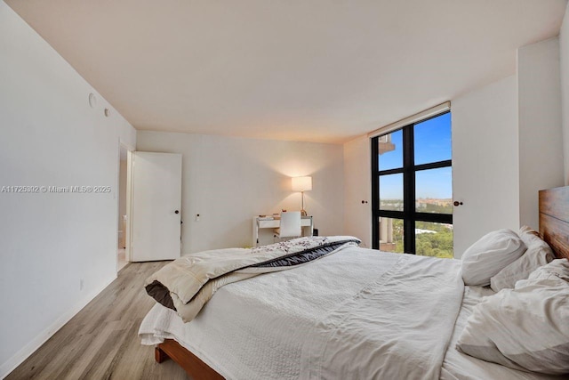 bedroom with a wall of windows and light hardwood / wood-style flooring