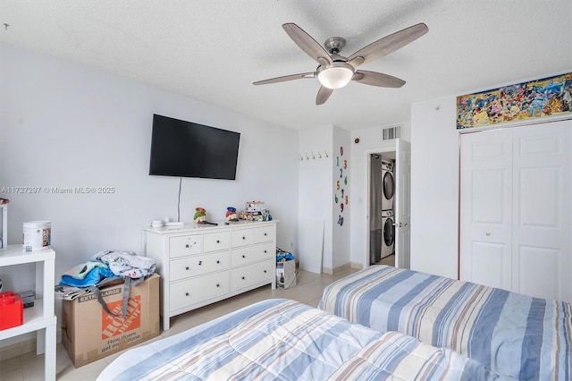 tiled bedroom with a textured ceiling, a closet, stacked washer / dryer, and ceiling fan