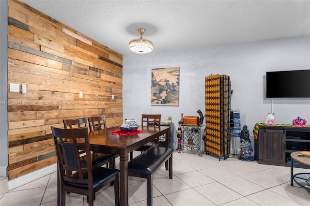 dining space with a textured ceiling, wood walls, and light tile patterned flooring