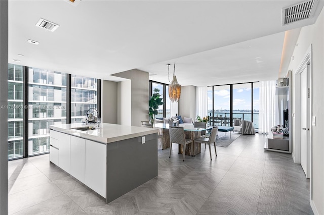 kitchen featuring sink, white cabinetry, expansive windows, a kitchen island with sink, and a water view