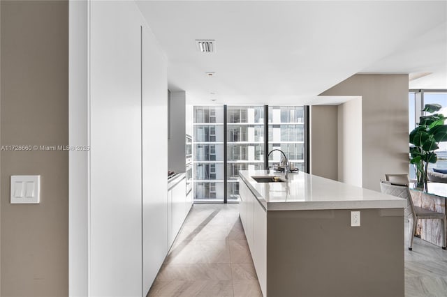 kitchen featuring white cabinetry, floor to ceiling windows, a center island with sink, and sink