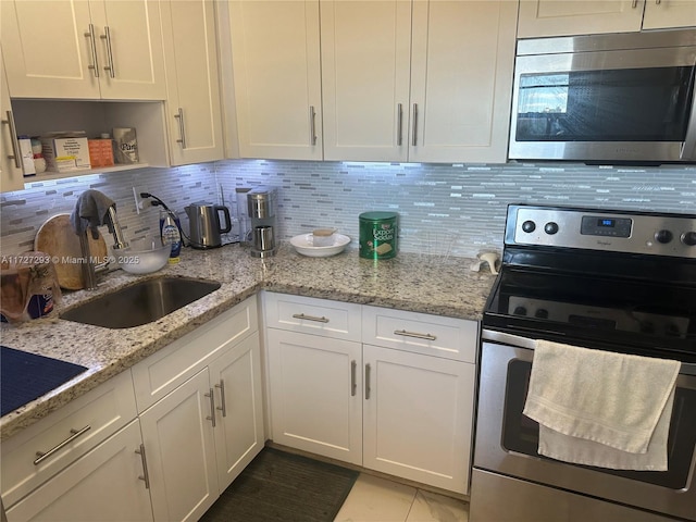 kitchen featuring white cabinetry, appliances with stainless steel finishes, backsplash, light stone countertops, and sink