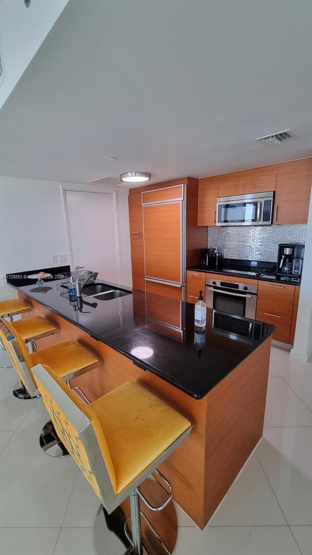 kitchen featuring light tile patterned floors, a kitchen bar, appliances with stainless steel finishes, and decorative backsplash