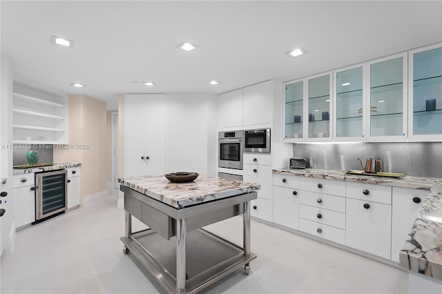 kitchen featuring white cabinets, light stone countertops, stainless steel oven, and beverage cooler