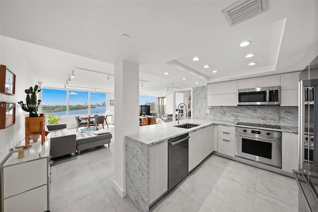 kitchen featuring kitchen peninsula, appliances with stainless steel finishes, tasteful backsplash, track lighting, and sink