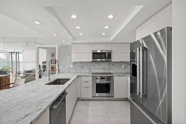 kitchen with light stone countertops, stainless steel appliances, a raised ceiling, and sink