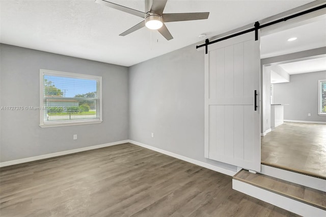 spare room with ceiling fan, a barn door, and hardwood / wood-style floors