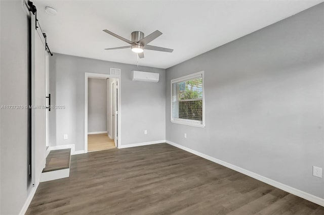 unfurnished bedroom featuring a barn door, ceiling fan, ensuite bath, dark wood-type flooring, and an AC wall unit