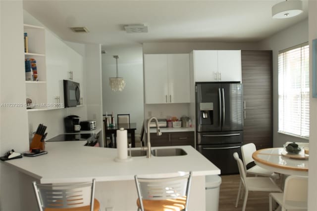 kitchen with black appliances, white cabinetry, sink, hanging light fixtures, and kitchen peninsula