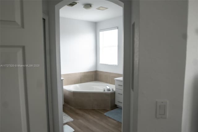 bathroom featuring vanity, wood-type flooring, and tiled tub