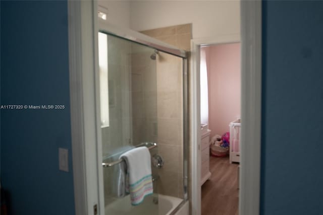 bathroom with bath / shower combo with glass door and wood-type flooring