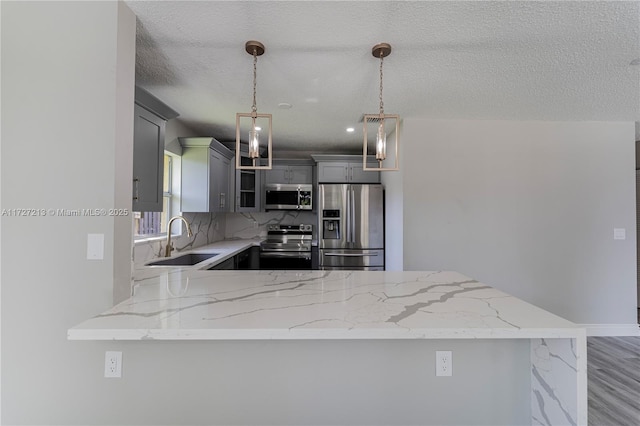 kitchen with a textured ceiling, decorative light fixtures, stainless steel appliances, sink, and kitchen peninsula