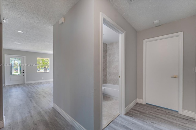 hall featuring light wood-type flooring and a textured ceiling