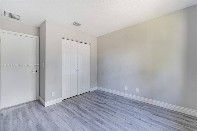 unfurnished bedroom featuring a textured ceiling, a closet, and light wood-type flooring