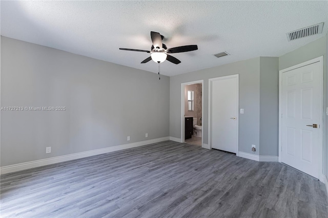 unfurnished bedroom featuring ceiling fan, a textured ceiling, hardwood / wood-style flooring, and ensuite bath