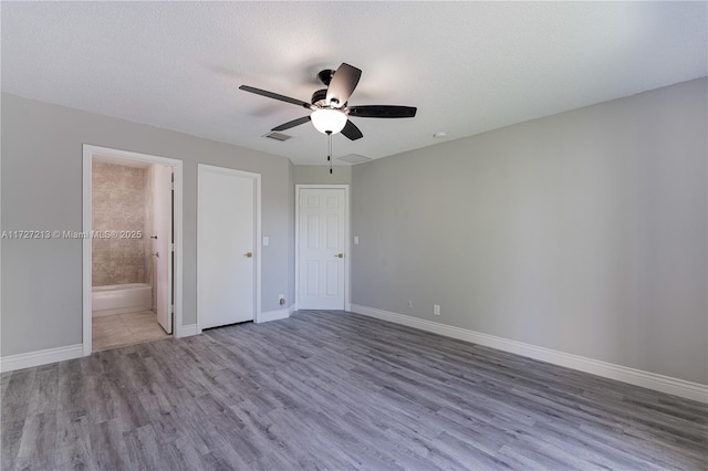 unfurnished bedroom with ceiling fan, hardwood / wood-style floors, connected bathroom, and a textured ceiling