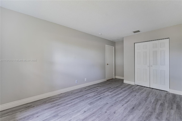 unfurnished bedroom with a textured ceiling, a closet, and light hardwood / wood-style flooring