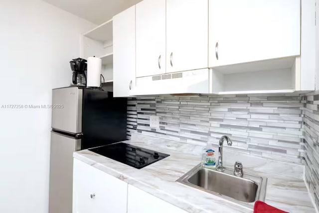 kitchen featuring white cabinetry, black electric stovetop, sink, backsplash, and stainless steel refrigerator