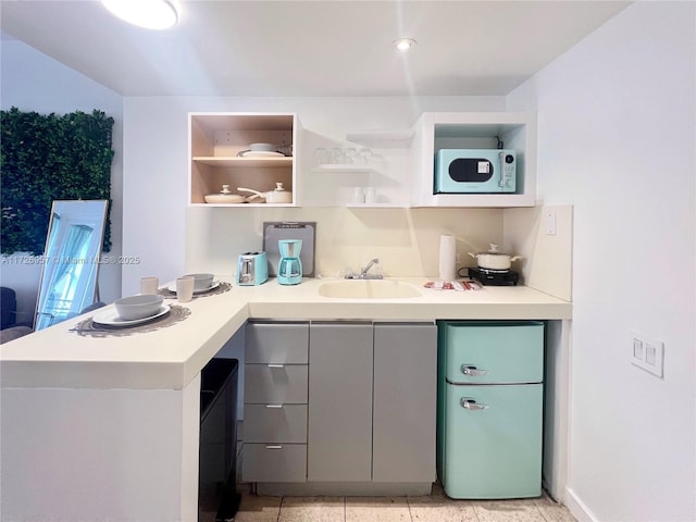 kitchen with light tile patterned flooring, gray cabinetry, kitchen peninsula, and sink