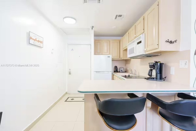 kitchen with light tile patterned floors, kitchen peninsula, a kitchen breakfast bar, and white appliances