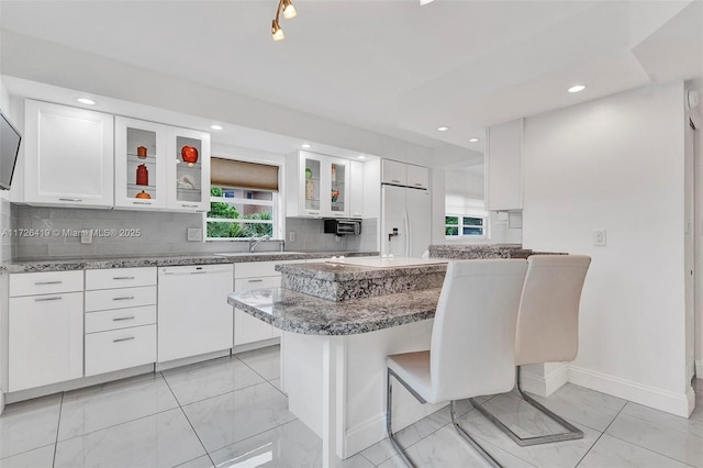 kitchen featuring a wealth of natural light, white cabinets, a kitchen breakfast bar, and white appliances