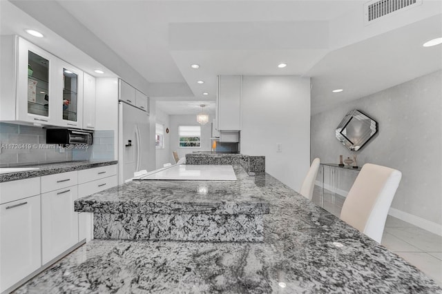 kitchen with white cabinetry, white fridge with ice dispenser, kitchen peninsula, and dark stone countertops