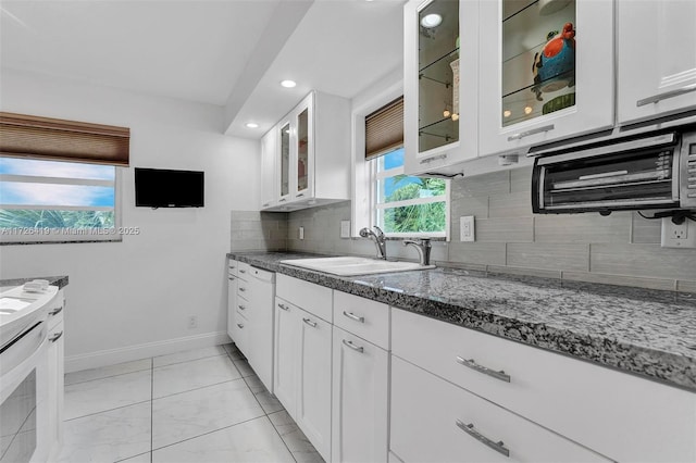 kitchen featuring dishwasher, dark stone countertops, decorative backsplash, sink, and white cabinets