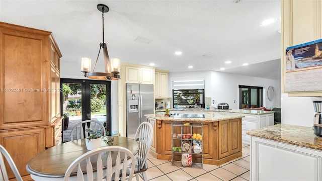 kitchen with kitchen peninsula, stainless steel refrigerator with ice dispenser, hanging light fixtures, light stone counters, and a center island