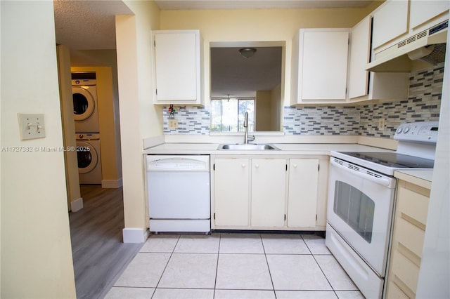 kitchen featuring light tile patterned floors, white appliances, stacked washer / dryer, white cabinets, and sink