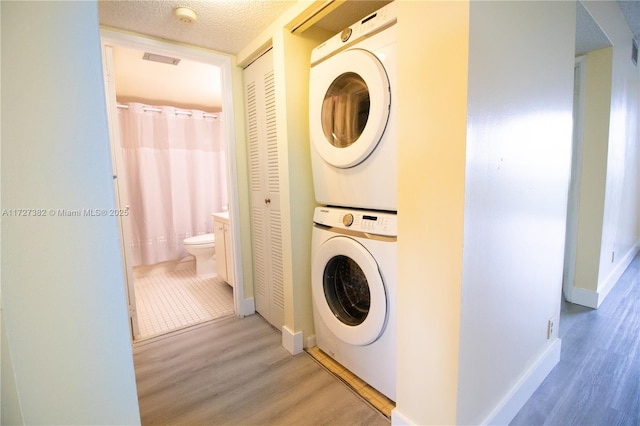 laundry area featuring stacked washing maching and dryer, a textured ceiling, and light hardwood / wood-style floors