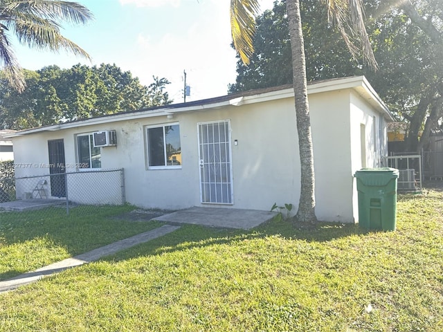 ranch-style home with a front yard, fence, a wall mounted AC, and stucco siding