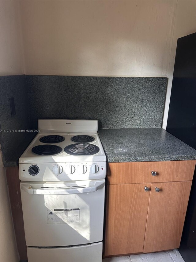 kitchen featuring black refrigerator, backsplash, white electric range oven, and light tile patterned flooring