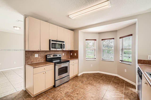 kitchen featuring cream cabinets, appliances with stainless steel finishes, a textured ceiling, light tile patterned floors, and decorative backsplash