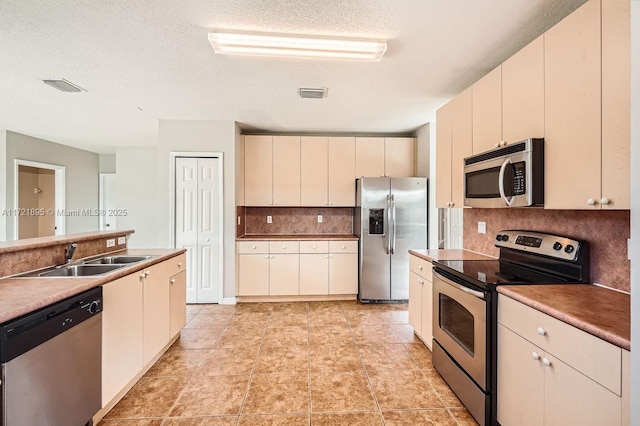 kitchen with a textured ceiling, appliances with stainless steel finishes, tasteful backsplash, sink, and cream cabinetry