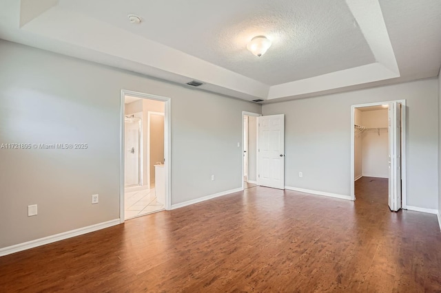 unfurnished bedroom with ensuite bathroom, wood-type flooring, a tray ceiling, and a walk in closet