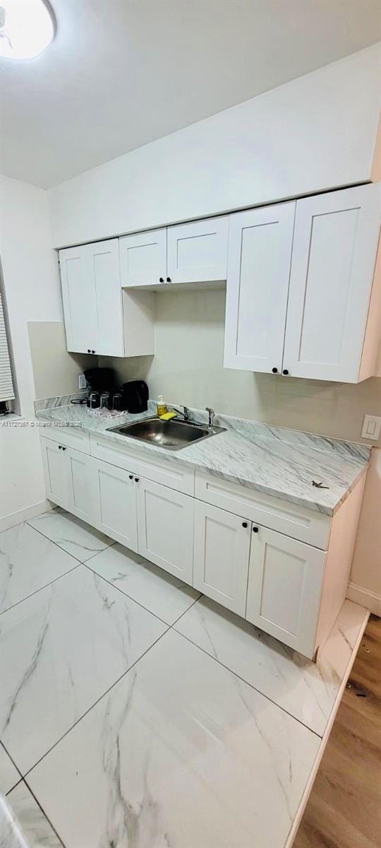 kitchen with light stone counters, sink, and white cabinets