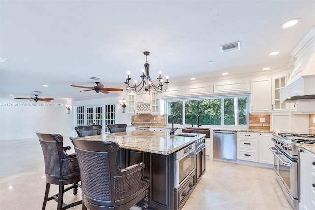 kitchen with white cabinetry, a kitchen bar, an island with sink, appliances with stainless steel finishes, and decorative light fixtures