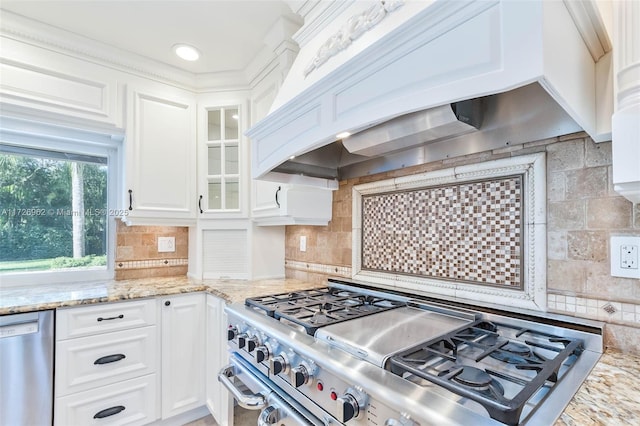 kitchen featuring backsplash, appliances with stainless steel finishes, custom range hood, white cabinets, and light stone counters