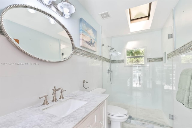 bathroom with vanity, a skylight, tile walls, toilet, and a shower with shower door