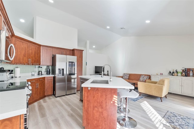 kitchen featuring a kitchen island with sink, stainless steel appliances, light hardwood / wood-style floors, decorative backsplash, and vaulted ceiling