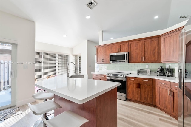 kitchen featuring an island with sink, appliances with stainless steel finishes, a kitchen breakfast bar, and sink