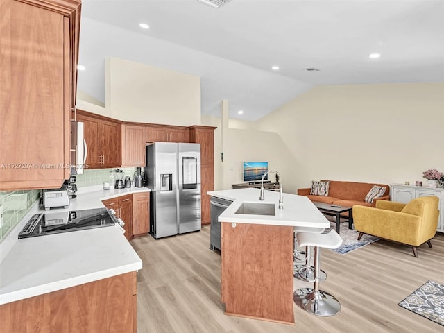 kitchen with lofted ceiling, appliances with stainless steel finishes, a kitchen island with sink, tasteful backsplash, and light hardwood / wood-style floors