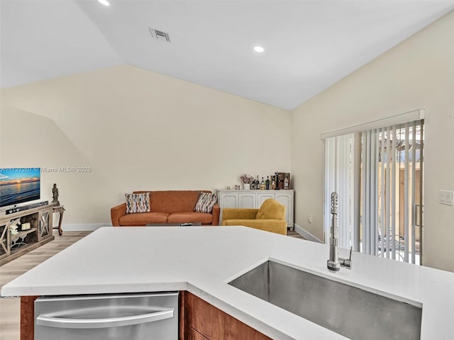 kitchen featuring vaulted ceiling, sink, stainless steel dishwasher, and light hardwood / wood-style floors