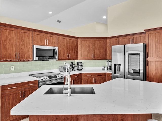 kitchen with lofted ceiling, sink, appliances with stainless steel finishes, light stone countertops, and a center island with sink