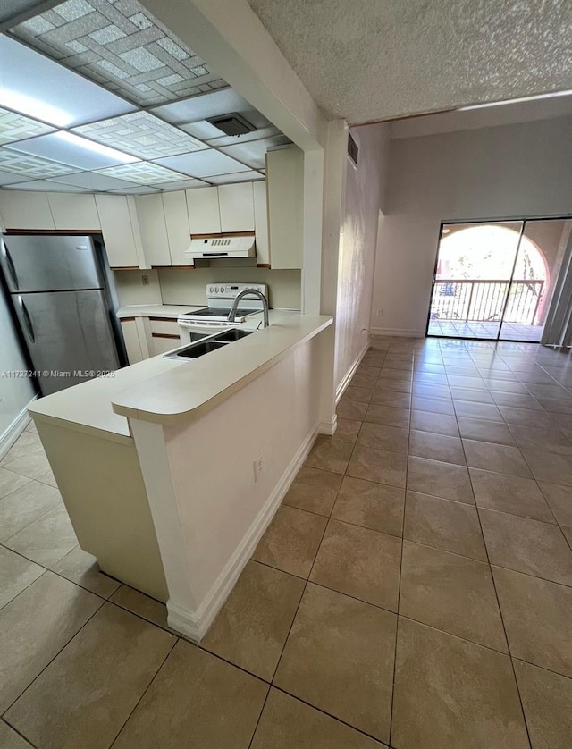 kitchen with white range with electric stovetop, kitchen peninsula, sink, stainless steel refrigerator, and white cabinetry