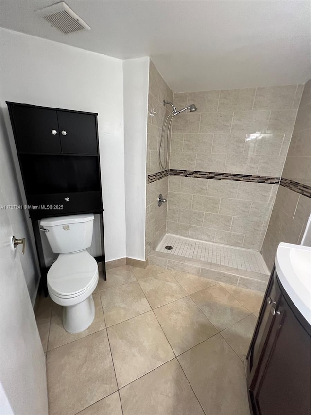 bathroom with toilet, tiled shower, vanity, and tile patterned flooring