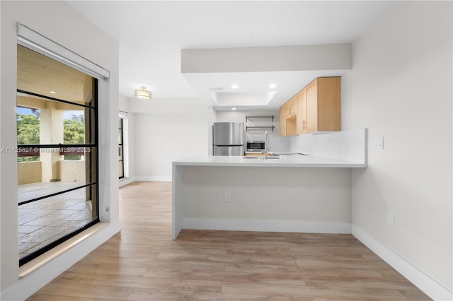 kitchen featuring light brown cabinetry, sink, stainless steel refrigerator, kitchen peninsula, and light wood-type flooring