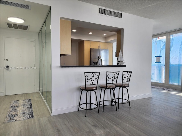 kitchen featuring plenty of natural light, a wall of windows, light hardwood / wood-style flooring, and stainless steel fridge