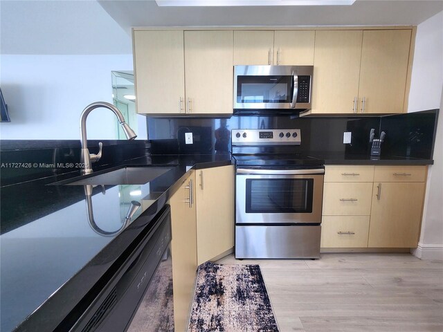 kitchen with stainless steel appliances, cream cabinets, sink, and light hardwood / wood-style floors